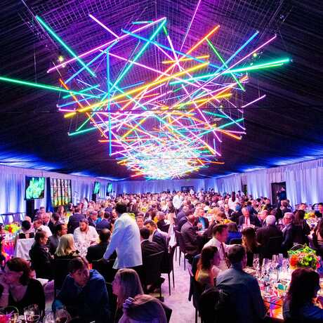 Interior of tent with colorful neon mobile and guests dining at Big Bang Gala