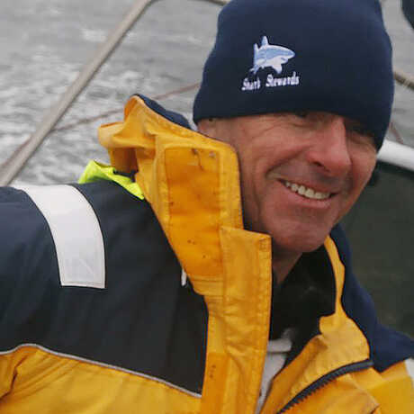Dressed in a bright yellow windbreaker, David McGuire sits on a boat in stormy weather smiling