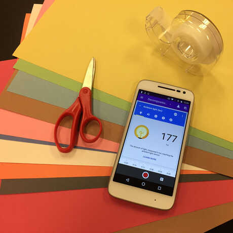 A smartphone, scissors, and scotch tape atop multicolored construction paper